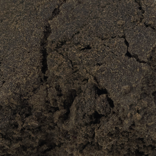 Nærbillede af mørk, tætpresset hash med en let skinnende overflade og tydelig struktur af fine trichomer.