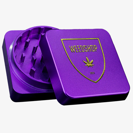 Lilla firkantet metalgrinder med guld Weedshop-logo på låget – elegant og eksklusivt design i Limited Halloween Edition.